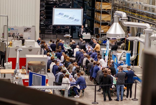 Barbaratag 2022. Der Blick von oben in die Fraunhofer IGCV versuchshalle zeigt die Teilnehmer an Biertischgarnituren zwischen den Forschungsanlagen sitzend.