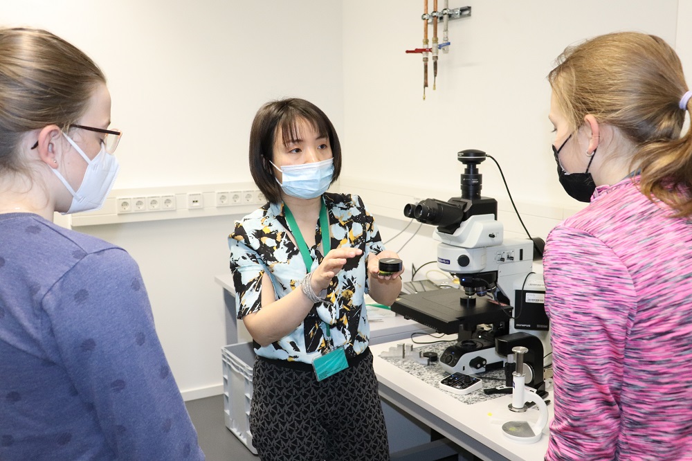 Fangtian Deng erläutert den Mädchen wie die Wissenschaftler mit dem Mikroskop arbeiten